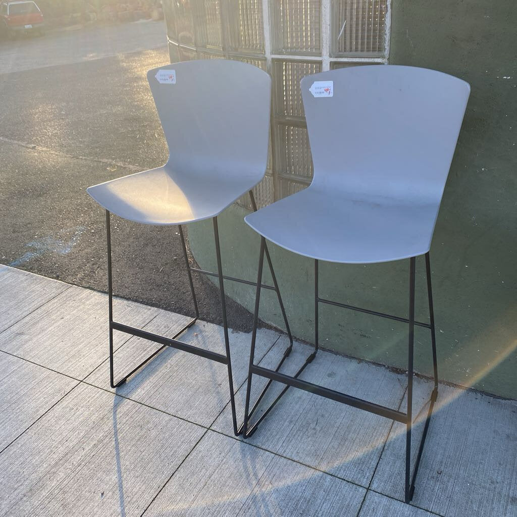 Two gray bar stools with black metal legs on a tiled floor.