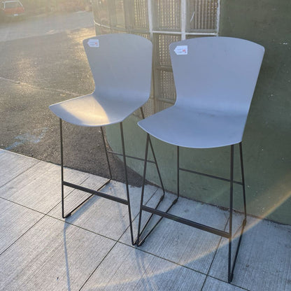 Two gray bar stools with black metal legs on a tiled floor.