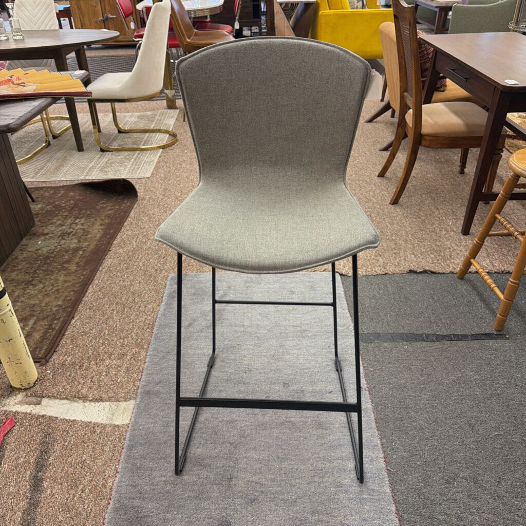 Gray bar stool with black legs on a gray rug in a room with tables and chairs.