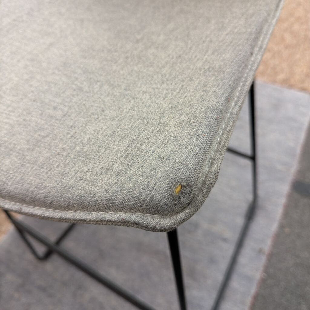 Close-up of a textured gray chair seat with a small yellow stain on a concrete floor.