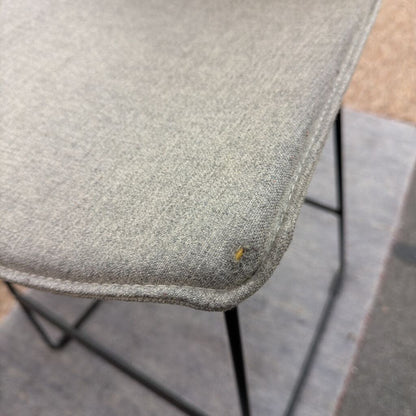 Close-up of a textured gray chair seat with a small yellow stain on a concrete floor.