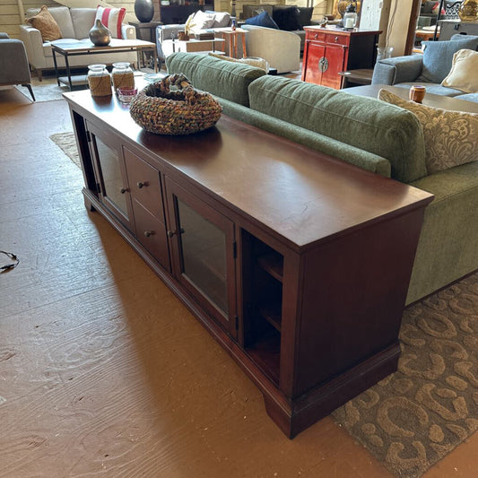 Wooden entertainment console in a living room setting with a green sofa and decorative items.