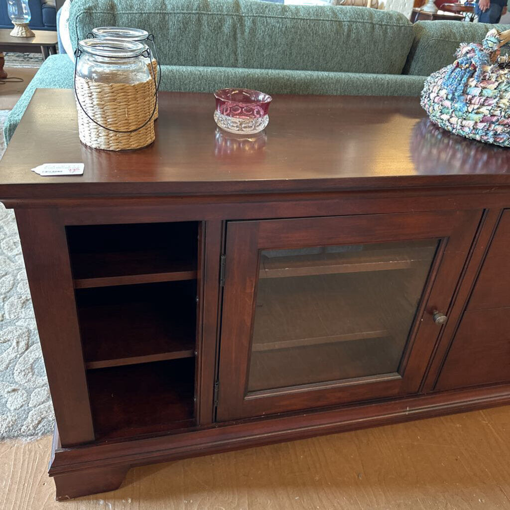 Wooden entertainment console with glass cabinet and decorative items on a living room floor.
