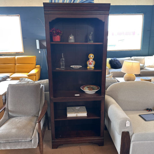 Wooden bookshelf in a living room with furniture and decor items.