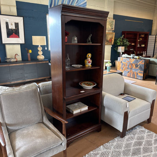 Wooden bookshelf in a living room with gray chairs and decorative items.