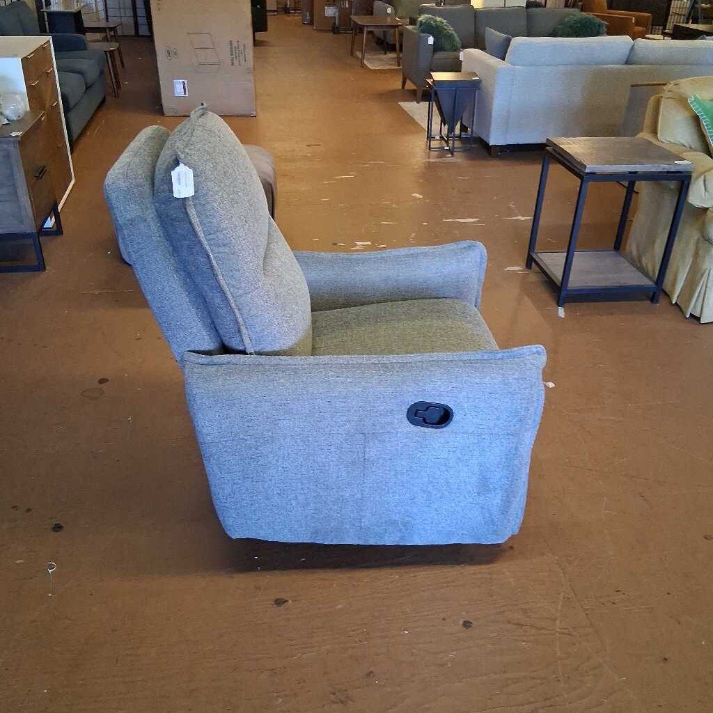 Gray recliner chair in a furniture store setting with other furniture items in the background.