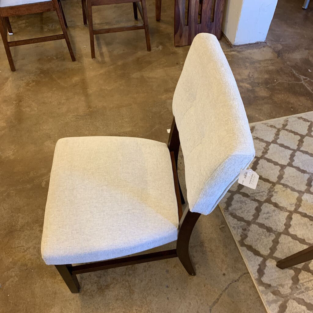 Pair of beige upholstered chairs on a brown floor with a patterned rug.