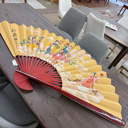 Traditional Chinese fan with colorful illustrations on a wooden table