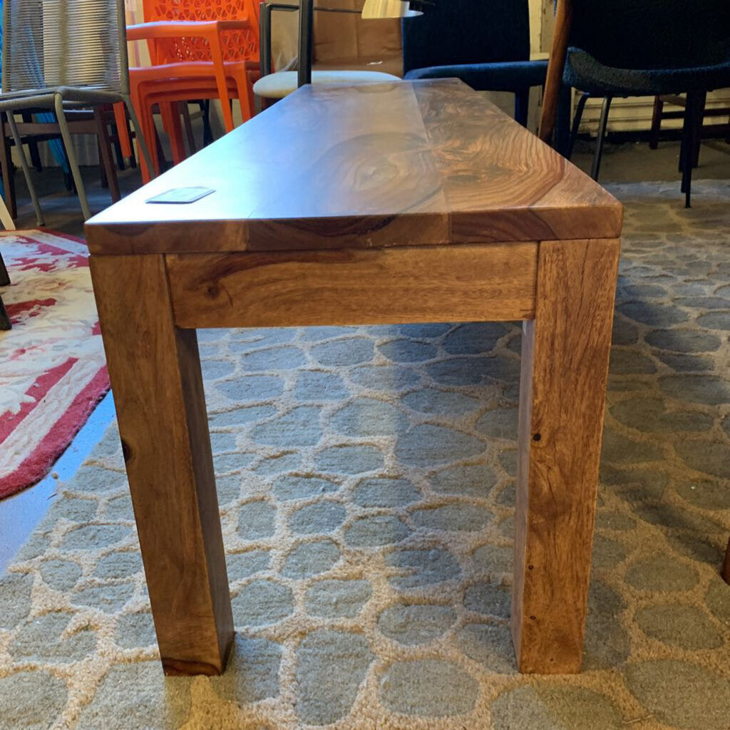 Wooden table on a patterned carpet with chairs in the background