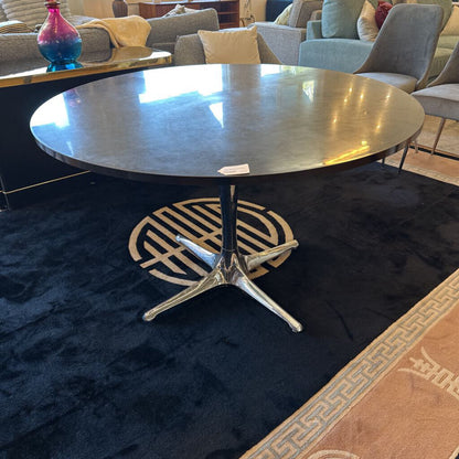 Round metal table with a black base in a room with chairs and a rug.
