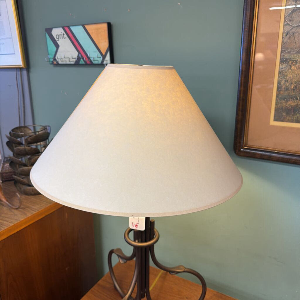 Lamp with a beige shade on a wooden surface against a green wall with framed pictures.