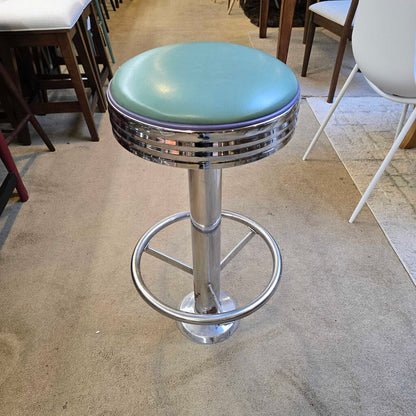 Bar stool with green cushioned seat and metal base in a room setting