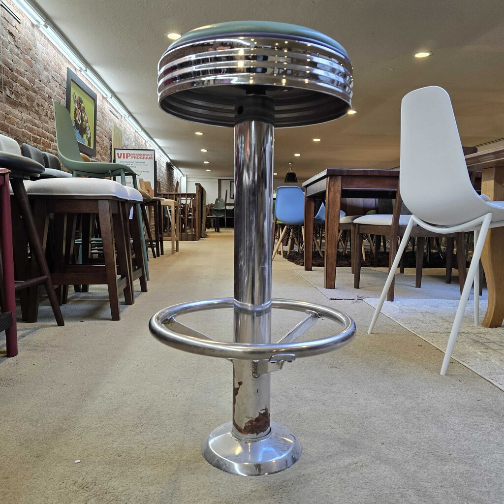 Bar stool with green cushioned seat and metal base in a room setting