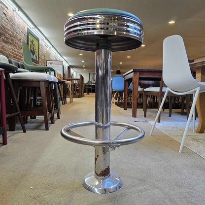 Bar stool with green cushioned seat and metal base in a room setting