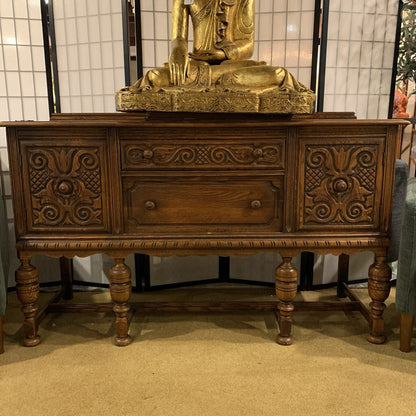 Wooden sideboard with intricate carvings and a gold Buddha statue on top.