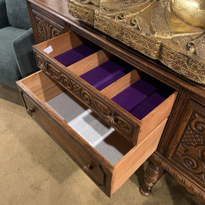 Wooden drawer with purple items inside, next to a large ornate statue.