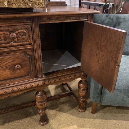 Wooden sideboard with open cabinet door next to a gray chair.