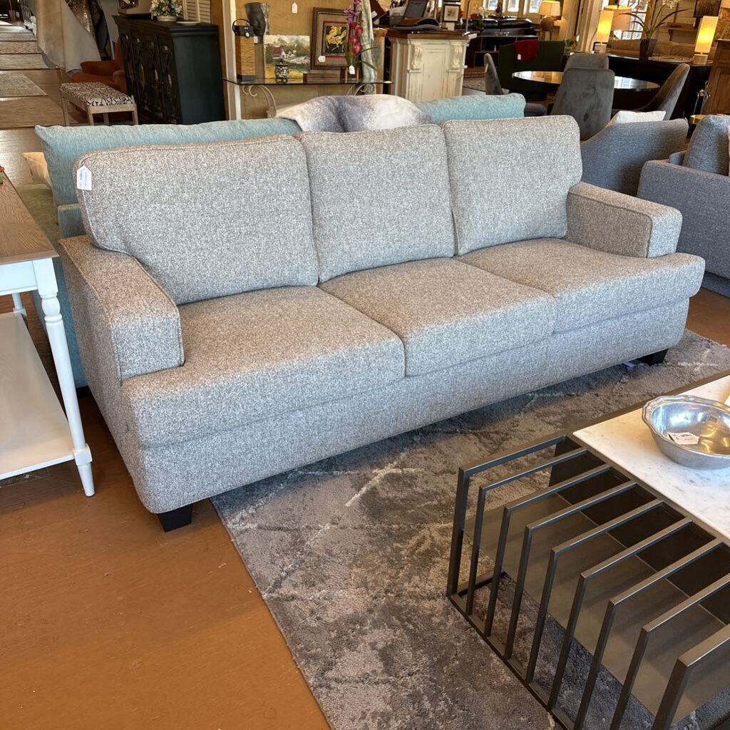 Gray sofa in a furniture store setting with other furniture items around.