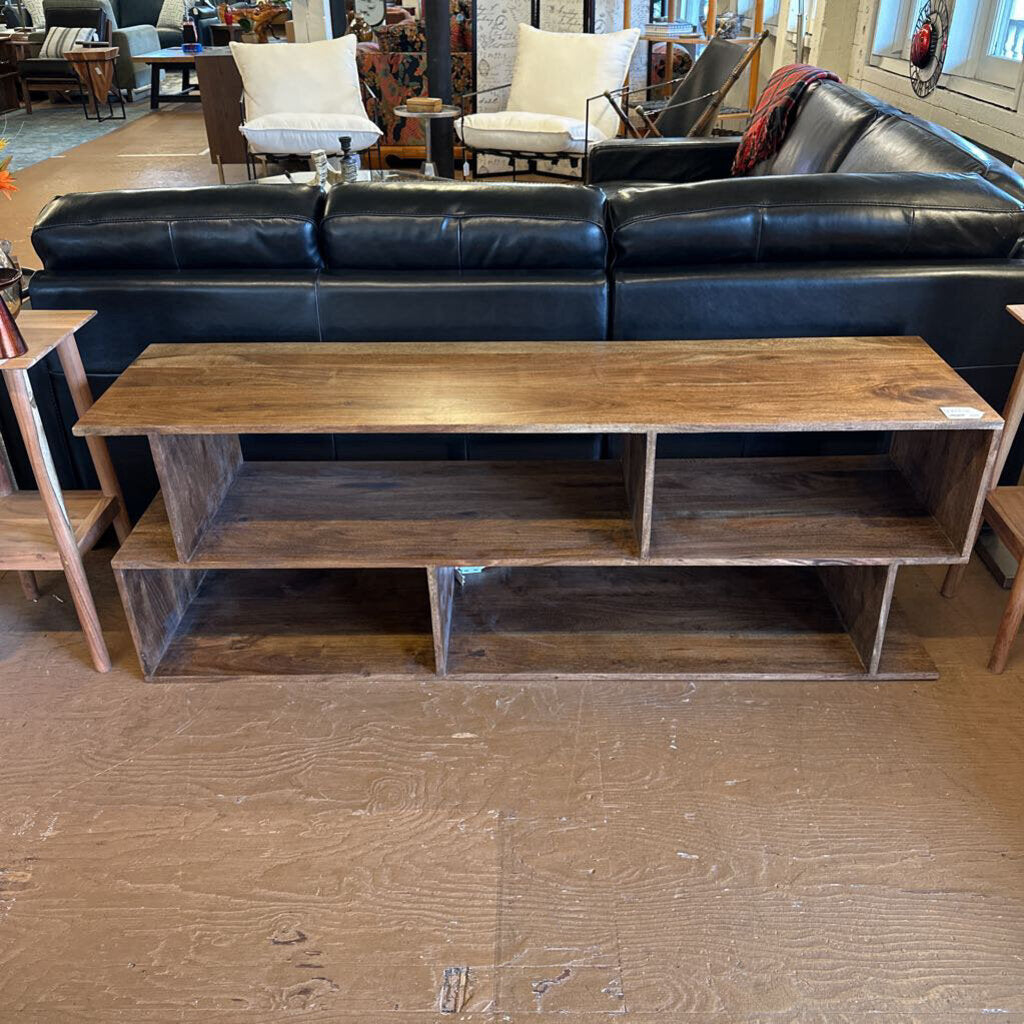 Wooden TV stand in front of a black leather sofa in a showroom setting.