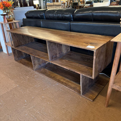 Wooden TV stand in a room with a black leather sofa and decorative items.