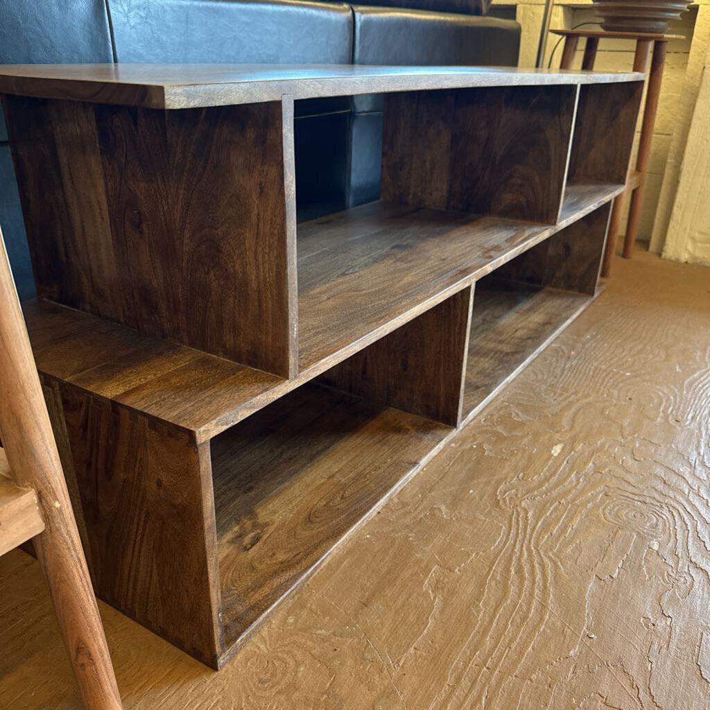 Wooden entertainment console against a wall with a couch in the background