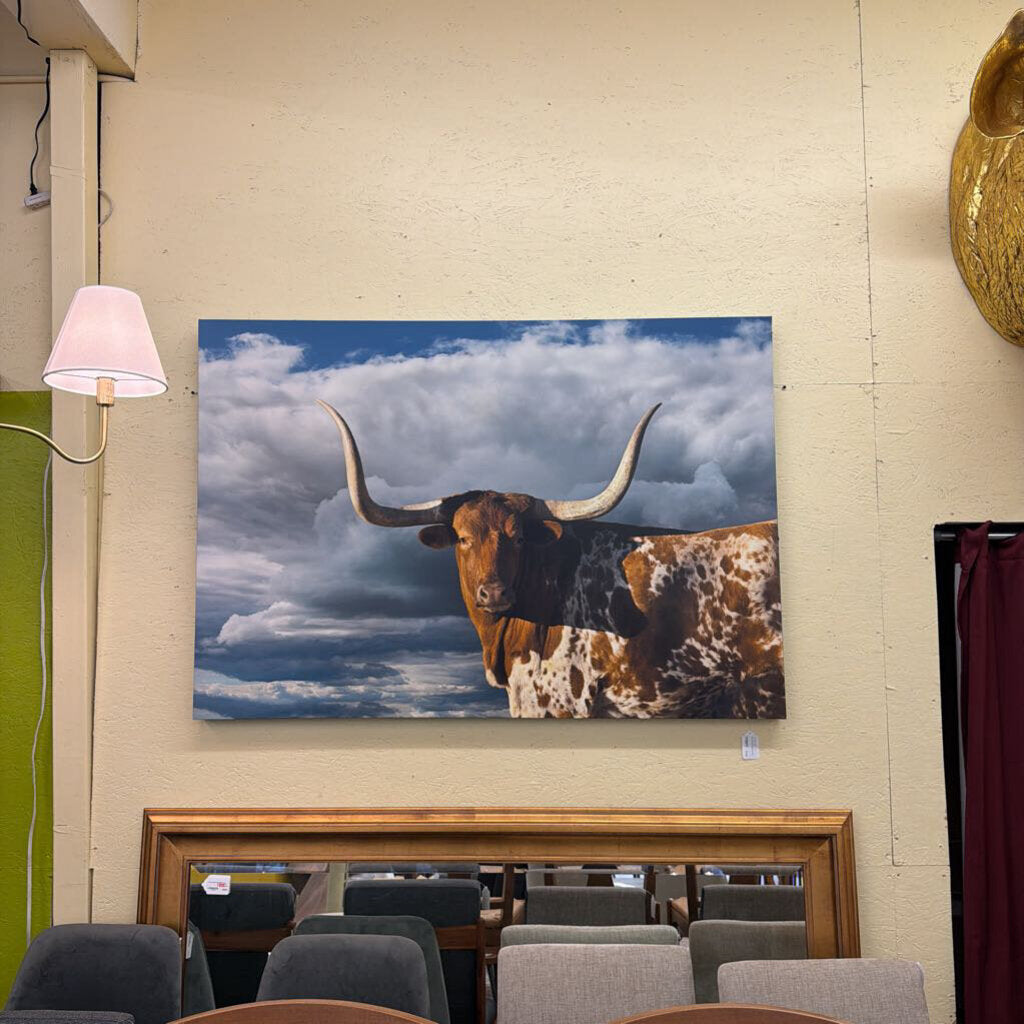 Longhorn cow painting on a wall above a wooden desk with chairs.