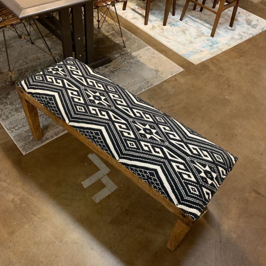 Wooden bench with a black and white patterned cushion in a room with a rug and chair.