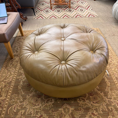 Round beige ottoman on a patterned rug in a room with a laptop and chair.