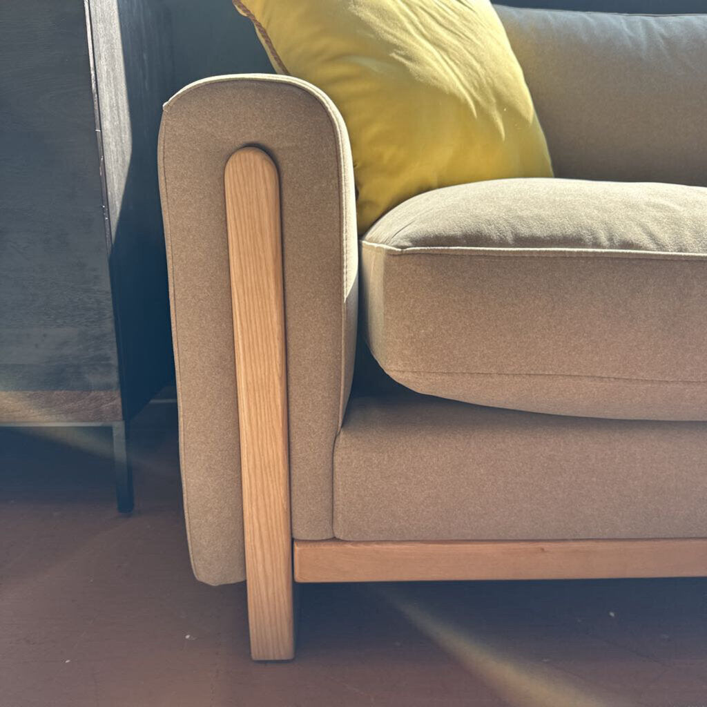 Beige sofa with wooden armrests and a yellow cushion on a dark floor.