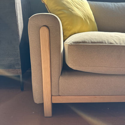 Beige sofa with wooden armrests and a yellow cushion on a dark floor.