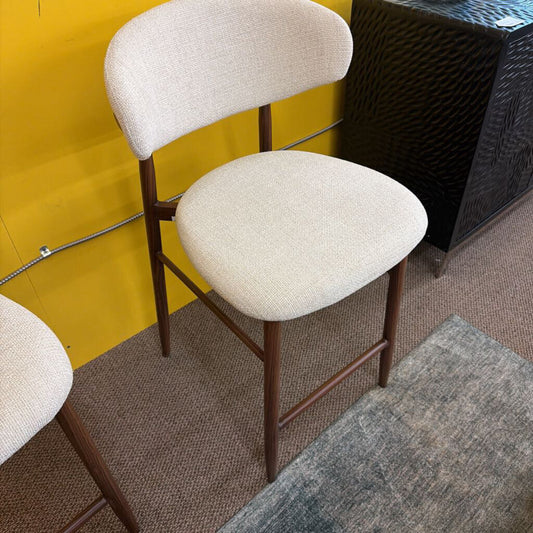 Beige bar stools with brown frames against a yellow wall.