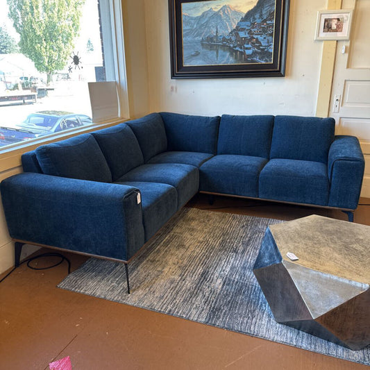 Blue sectional sofa in a living room with a coffee table and window view.