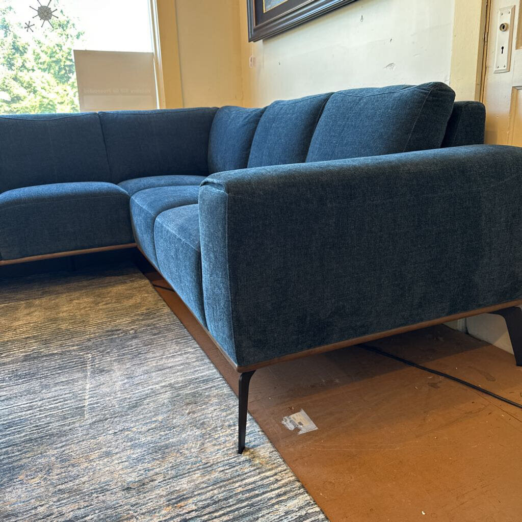 Blue sectional sofa in a room with a carpeted floor and a door in the background.