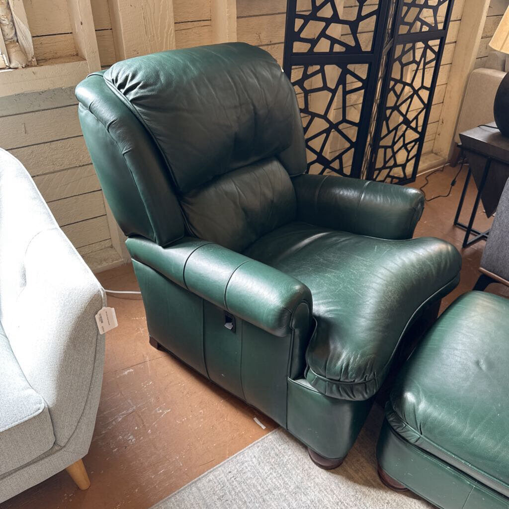 Green leather recliner chair in a room with wooden floor and wall.
