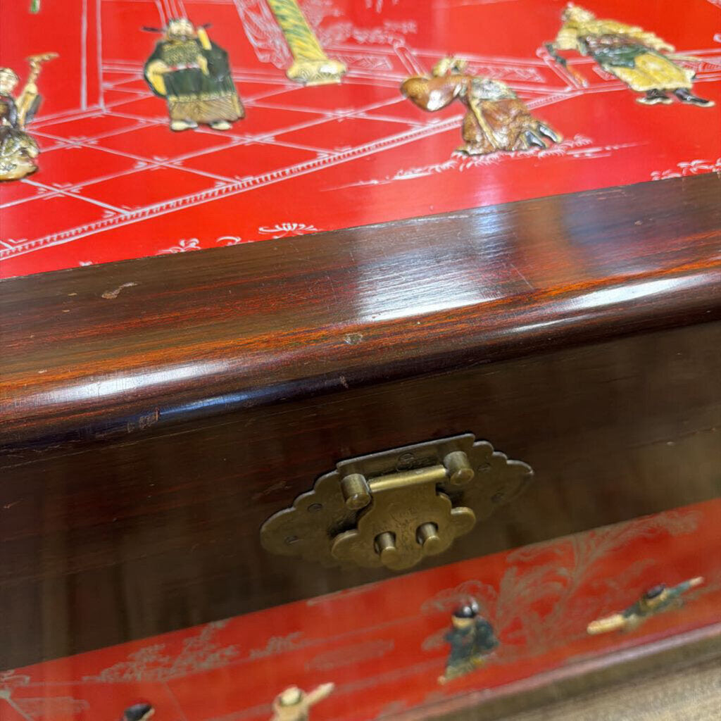 Wooden box with red decorative lid featuring gold figures and a brass latch.