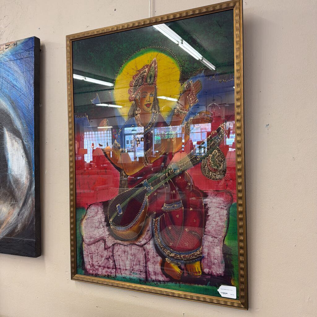 Framed artwork of a deity playing a stringed instrument on a beige wall.