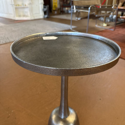 Small round metal table on a wooden floor with a blurred background