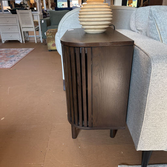 Wooden side table with a lamp on top next to a gray sofa in a room setting.