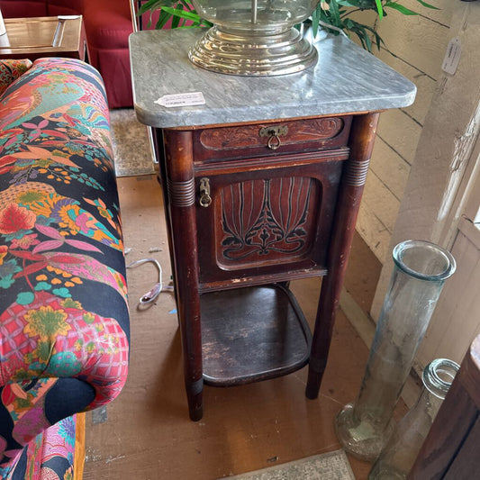 Vintage wooden side table with marble top in a room with colorful chair and glass vase.