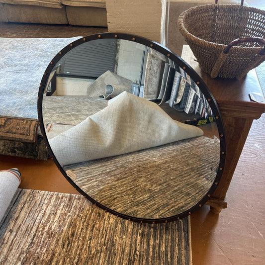 Round mirror reflecting a room with a table and chair.