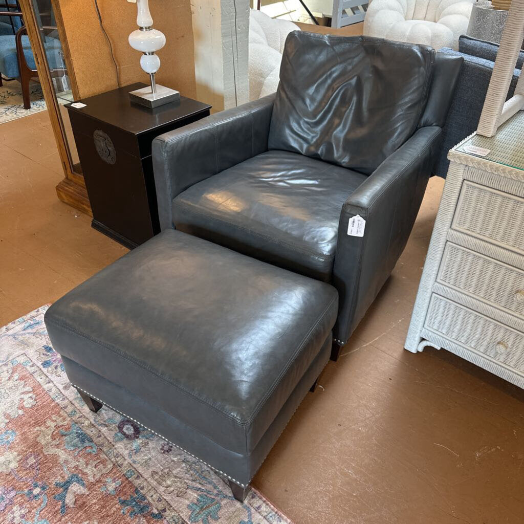 Gray leather armchair and ottoman on a brown floor with a patterned rug.