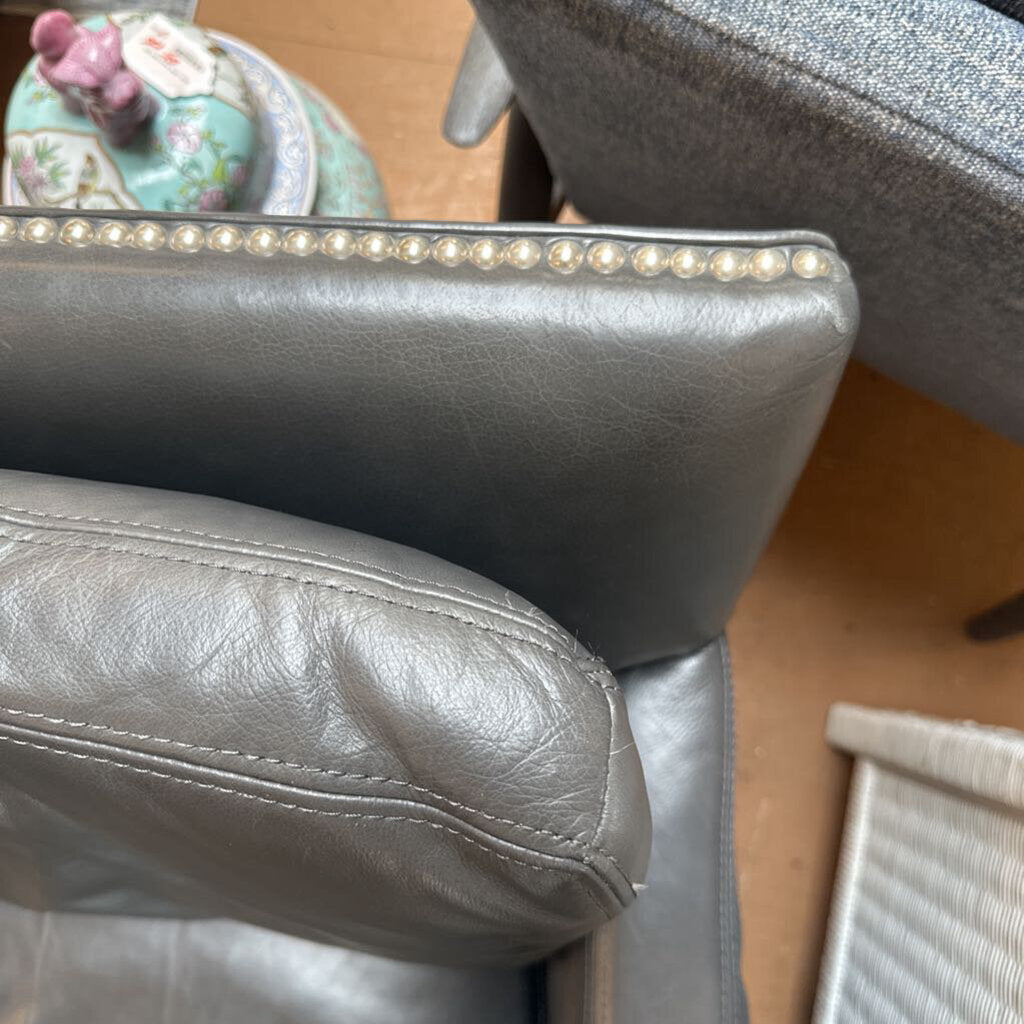Close-up of a gray leather chair with decorative elements on a wooden floor.