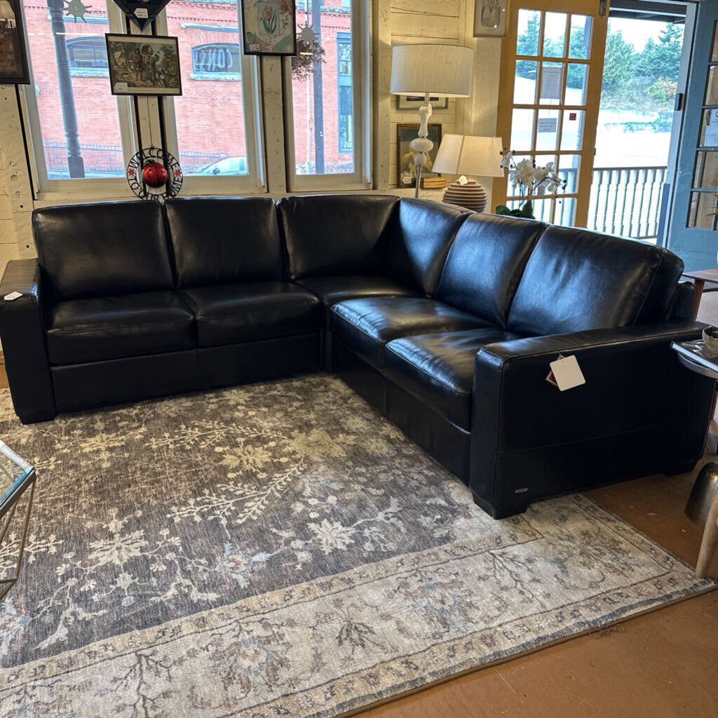 Black leather sectional sofa in a living room setting with a rug and decor.