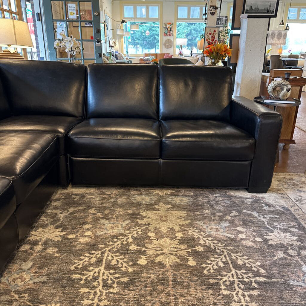 Black leather sectional sofa in a room with a patterned rug and decorative items.