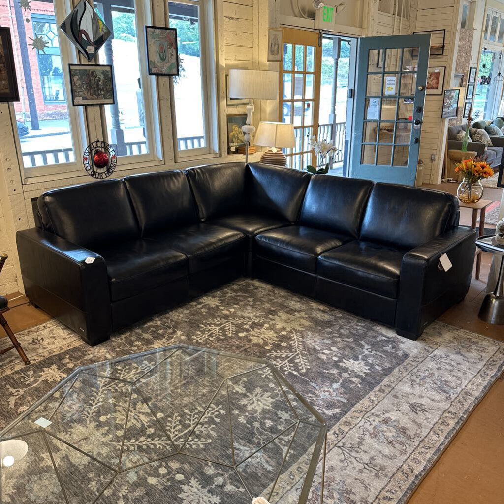 Black leather sectional sofa in a living room with a patterned rug and decorative items.