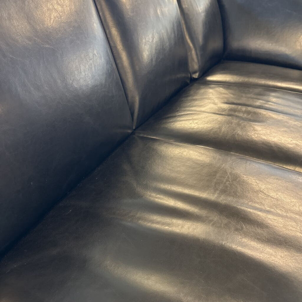 Corner of a black leather sofa with visible wear.