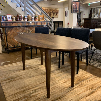 Wooden dining table in a showroom setting with chairs and decor.