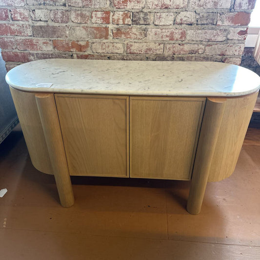 Wooden sideboard with marble top against a brick wall.