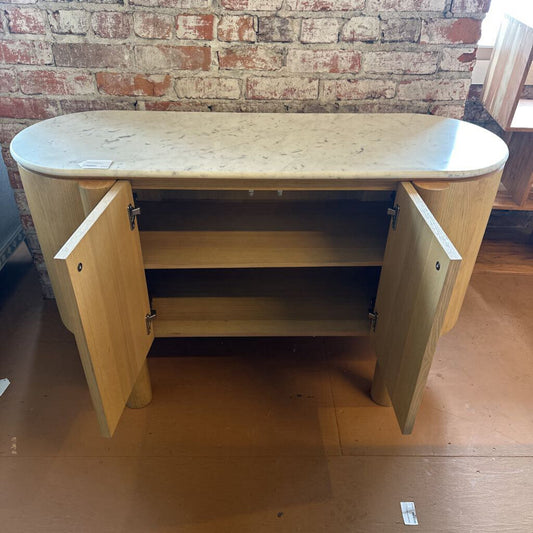 Wooden sideboard with open doors against a brick wall.