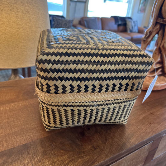 Woven basket with black and beige pattern on a wooden surface